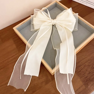 Close-up of elegant cream satin and organza bow hair clip with long ribbons on a velvet tray