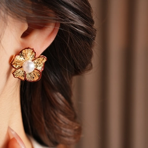 Detailansicht von Blumen-Ohrring mit Goldkanten und Perle am Ohr des Models