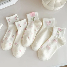 Detailed close-up of five pairs of white mid-calf socks with pink floral embroidery