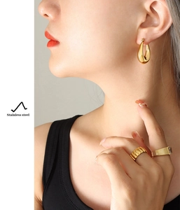 Close-up of gold-plated stainless steel U-shaped earrings and rings on a female model