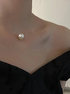 Close-up of a single white pearl pendant on a minimalist invisible necklace on collarbone