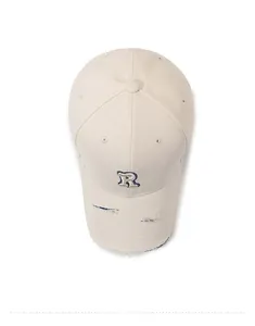 Macro view of distressed beige cotton baseball cap with blue embroidered letter R logo