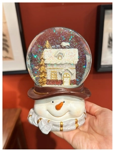 Detailed close-up of a snowman music box crystal ball with colorful glitters and golden trees