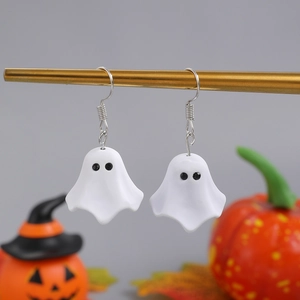 Close-up of ghost earrings made of white resin on gold stand with pumpkins