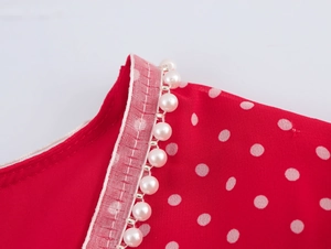 Dettaglio vestito rosso a pois con rifinitura in perle sullo scollo a V elegante