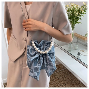 Detail view of light blue floral bucket bag with pearl handle and bow on a model