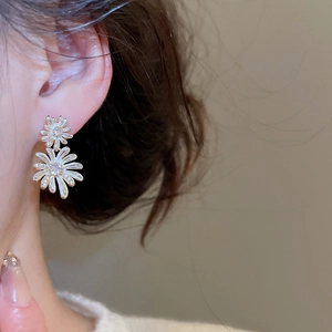 Close-up of elegant double-layered daisy drop earrings with white enamel and sparkling crystals