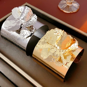 Close-up of gold and silver flower cuffs with textured metal finish on a dark tray