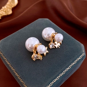 Close-up of pearl earrings with gold star and flower pendants on a green velvet box