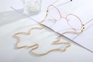Detail of beaded champagne gold eyewear chain with metal clasps on a white book