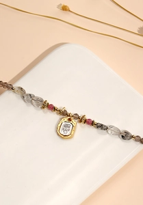 Detail of beaded necklace with gold relief pendant and natural black rutilated quartz