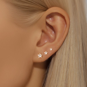 Close-up of three gold star stud earrings with white zircons on female ear lobe