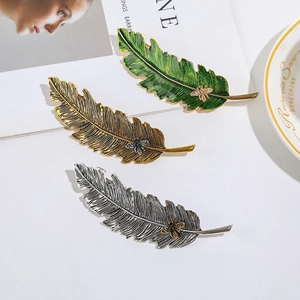 Three hollow leaf hair clips with bees in green, gold, and silver on a fashion magazine