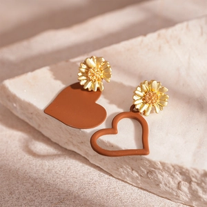 Detail of asymmetrical daisy earrings with matte brown heart pendants on stone