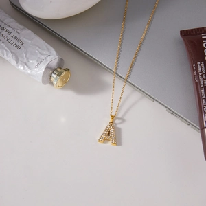 Goldene Kette mit Buchstabe A Anhänger und Strasssteinen auf modernem Schreibtisch