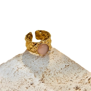 Irregular geometric gold ring with pink gemstone and rhombus pattern on stone background