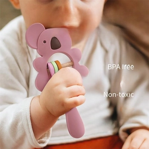 Pink silicone koala baby teether rattle with wooden handle being gripped and chewed by infant