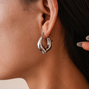 Close-up of polished silver hollow heart hoop earring worn by a model for a chic style