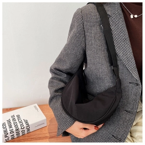 Close-up of a black nylon crescent bag with adjustable strap worn on a gray blazer