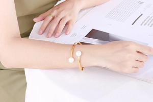 Minimalist gold open bangle featuring large double pearls worn on wrist for an elegant look