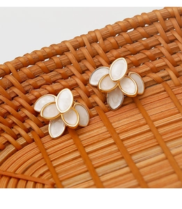 Detailed shot of gold-rimmed white petal earrings on a rustic woven tray with soft shadows