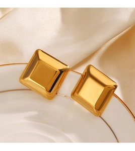 Polished gold square stud earrings displayed on a white plate with beige silk background