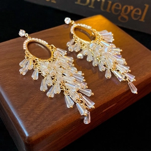 Close-up of golden tassel earrings with sparkling teardrop crystals on a dark wood surface