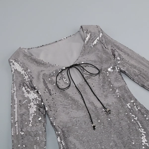 Détail de paillettes argentées sur robe à manches longues avec cordon noir et embouts