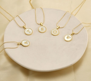 Detailed view of five golden shell alphabet necklaces on a white ceramic plate
