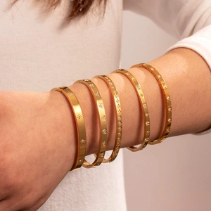 Minimalist gold titanium steel bangles with star heart and diamond patterns on model wrist