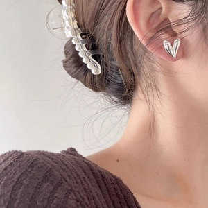 Detailed view of model wearing minimalist silver heart stud earrings and a pearl hair claw