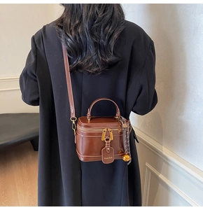 Rear view of model wearing a brown leather box bag with gold hardware and black coat