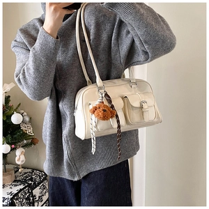 Detail view of a cream shoulder bag with front flap pockets and a cute bear charm accessory