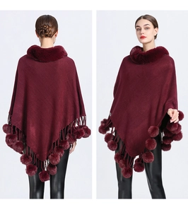 Detail of burgundy knit poncho with plush faux fur collar and decorative pom-pom tassels
