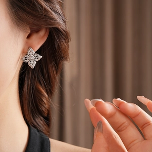 Close-up of hollow flower stud earrings with sparkling zircons worn by a model