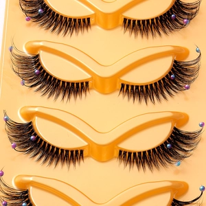 Dramatic fox-eye false eyelashes with colorful pearls on a yellow tray for stage makeup