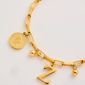 Detailed close-up of golden titanium steel bracelet with coin and letter Z charms