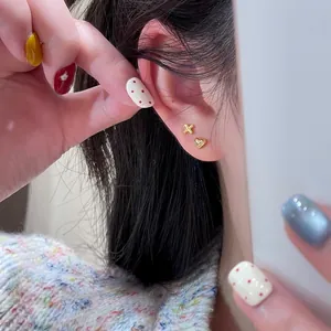 Close-up of small golden heart and cross stud earrings worn on a model's earlobe