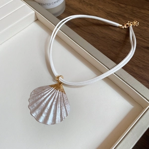 Detail of white double-cord necklace with golden seashell pendant on a display tray