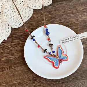 Detail view of colorful ceramic butterfly pendant on brown woven rope necklace