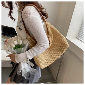 Close-up of a woven straw beach bag with brown leather straps held by a model in casual outfit