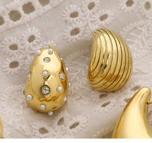 Close-up of 18K gold teardrop earrings with pearls and striped shell textures on lace