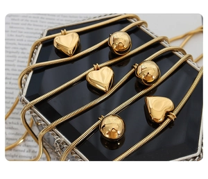 Detail of gold snake chain necklace featuring heart and sphere pendants on jewelry box