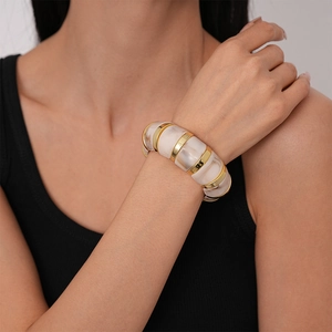 Detail of wide cream marble acrylic stretch bracelet with gold rings on woman's wrist