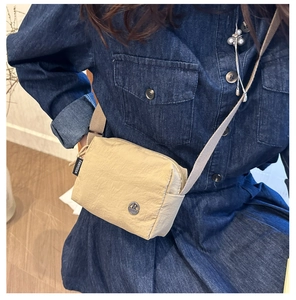 Close-up of beige nylon crossbody bag featuring adjustable strap and metallic logo detail