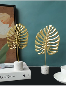 Detail of golden monstera leaf metal sculptures on white terrazzo base for modern home decor