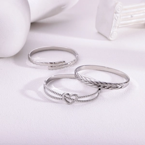 Three minimalist silver stainless steel bracelets with heart and geometric textures on white