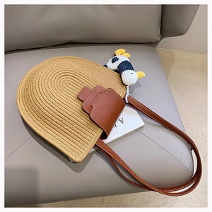 Close-up of semi-circle woven cotton bag with brown leather strap and duck charm
