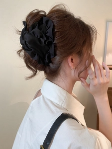 Detail of a large black pleated fabric flower hair clip worn by a model in a side view