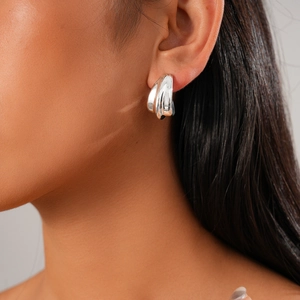 Détail de boucles d'oreilles créoles argentées multicouches au fini métal brillant